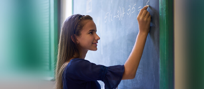 Student writing math problems on chalkboard